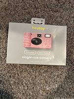 Front view of Heyday single-use camera with pink abstract swirly pattern in original packaging, showing product branding and camera design.