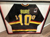 Full view of the framed black Vancouver Canucks jersey with yellow and red striping, displaying the name BURE and number 10, under glass.