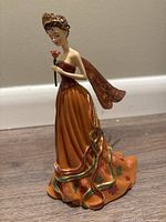 Front view of the Queen of the Autumn Equinox figurine showing detailed facial features, dress and flower held in hand.