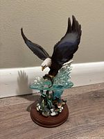 Porcelain bald eagle figurine swooping down over water with aquatic plants on wooden base, shown from front angle