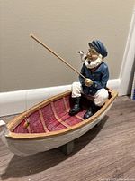 Front view of the old salt fisherman figurine sitting in a wooden boat, showing details of the fisherman holding fishing rod and the small bird on his shoulder.