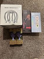 Photo showing all lot items: boxed electric head massager, boxed facial mister, boxed hair twister, and two boxed purple mini detangle brushes.