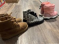 Three pairs of children's boots including the tan UGG ankle boots, leopard print boots, and pink winter boots for comparison.