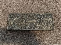 Top view of the closed jewelry box showing intricate floral metal engraving on lid.