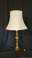 Front view of brass table lamp with white traditional lampshade on black background.