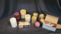 Full lot of 11 assorted candles including natural element candles, Christmas candles in brass holders, flameless and Partlite candles, and a cranberry pillar candle.