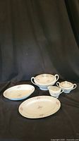 Five Chateau Rose fine china serving pieces arranged on black cloth backdrop. Includes tureens, gravy boat, bowl, platter with rose floral patterns and gold trim.