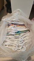 Top-down view of a large bundle of white plastic clothes hangers held together in a clear plastic bag, some with colored fabric strips on the bar to prevent slipping.