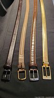 Four genuine leather belts laid out side by side showing colors and buckles