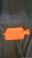 Orange hot water bottle laid flat showing overall condition against dark fabric
