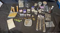 Overview of the jewellery making supplies including beads, cords, threads, pins, and charms arranged on black surface.