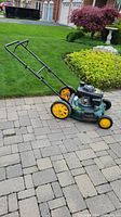 Full view of lawn mower on paved driveway showing green deck, yellow wheels, black handle