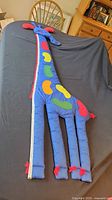 Full length view of fabric giraffe measuring tool laid out on table showing colorful spots and tape measure edge