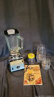 Full lot showing Osterizer blender base, glass jar, smoothie maker attachment, coffee grinder with yellow lid, additional glass jar, and cookbook.