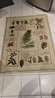 Full view of beige rectangular rug with framed fern, leaf, and berry patterns in green and mauve.