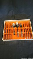 Full view of the 32-piece stainless steel flatware set in original box showing spoons, forks, and knives separated in orange compartments