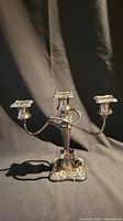 Front view of the silver candelabra showing three ornate candle holders and decorative base against black background