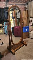Front view of solid oak full length oval mirror on base in indoor setting.