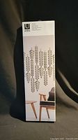 Tall rectangular box of Umbra 'Vines' decorative wall decor. Shows image of multiple vine designs on box front and modern living room setting.