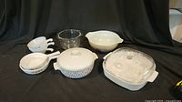 Nine various cooking and serving dishes including patterned ceramic bowls, clear and white glass baking dishes with lids, and clear glass mixing bowls.