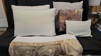 Photograph of all pillows arranged on dark fabric showing size, shape, and floral detailing on one pillow, also dust skirt draped in front