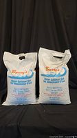 Front view of two white plastic bags of Barry's Water Softener Salt with handles at top placed against black background.