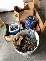 White bucket with heavy metal chains and large nails along with smaller buckets and boxes containing additional nails and spikes.
