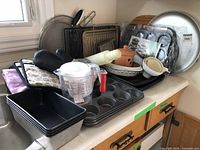 Various baking pans including loaf pans, muffin trays, pizza stone, oven mitts, measuring cup, ceramic garlic keeper, mixing bowl, baking sheets, cooling racks, and vacuum sealer.