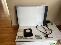 Light therapy lamp panel and black metal stand resting on BOXelite branded cardboard box