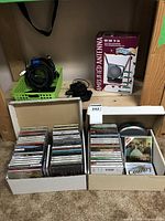 Boxes containing several dozen assorted music CDs and an amplified antenna box with cables on a shelf.