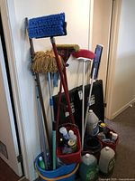 Photo showing multiple cleaning tools including mops, brooms, mop bucket with wringer, and various cleaning products.