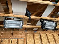 Two black Comfort Zone electric ceiling heaters mounted on wooden beams in a garage or workshop environment.