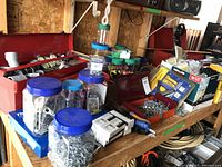 Workbench with multiple jars containing assortment of screws and other electrical components, cardboard boxes and organized parts.