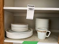 Corelle dishes stacked on a shelf including bowls, large plates, smaller plates, and a Pyrex mug with brown floral pattern.