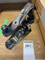 Photo showing two metal hand planes side by side on a wooden surface, one Craftsman brand with a blue painted base and the other Stanley brand with a black base.