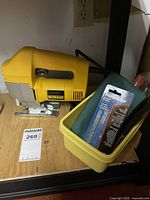 DeWalt DW313 jig saw, yellow plastic container with accessories including jig saw blades in packaging and loose blades.