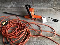 Full view of electric hedge trimmer laying on concrete floor with coiled orange extension cord