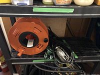 Orange extension cord reel and metal cage-protected trouble light on shelf