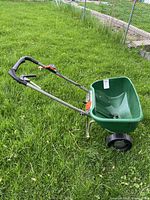Green Scotts fertilizer spreader on grass, showing handle, hopper and wheels