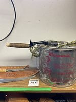 Fishing rod with cork handle, reel attached, next to metal minnow pail with Mermaid branding.