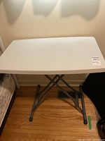 Full view of the white plastic folding table with gray metal legs.