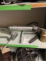 Two metal grease guns on a shelf, one barrel-style with hose, one lever-style.