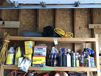 Wide shelf view with Homelite chainsaw bar case, yellow coiled cable, various brushes, cleaning liquids, and contractor trash bags.