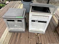 Two gray plastic hose reel storage boxes on wooden deck, one with lid open and one closed showing size difference and condition.