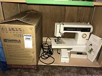 Kenmore 1251 sewing machine set inside wooden shelf next to its original box. Includes power cord, foot pedal, accessories box, and manual.