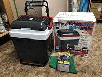 Koolatron portable cooler next to its original box, power adapter, and a green mesh bag containing accessories.