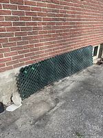 Several green resin lattice panels stacked against a red brick wall outside.