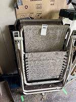 Folded anti-gravity lawn chairs stacked indoors showing fabric and frame details