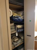 Photo showing shelving unit filled with various folded linens including blankets, bedding, and towels in a variety of colors and patterns.