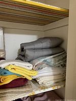 Shelf with grey quilted throw on top and multiple towels and linens folded underneath in various colors and sizes.